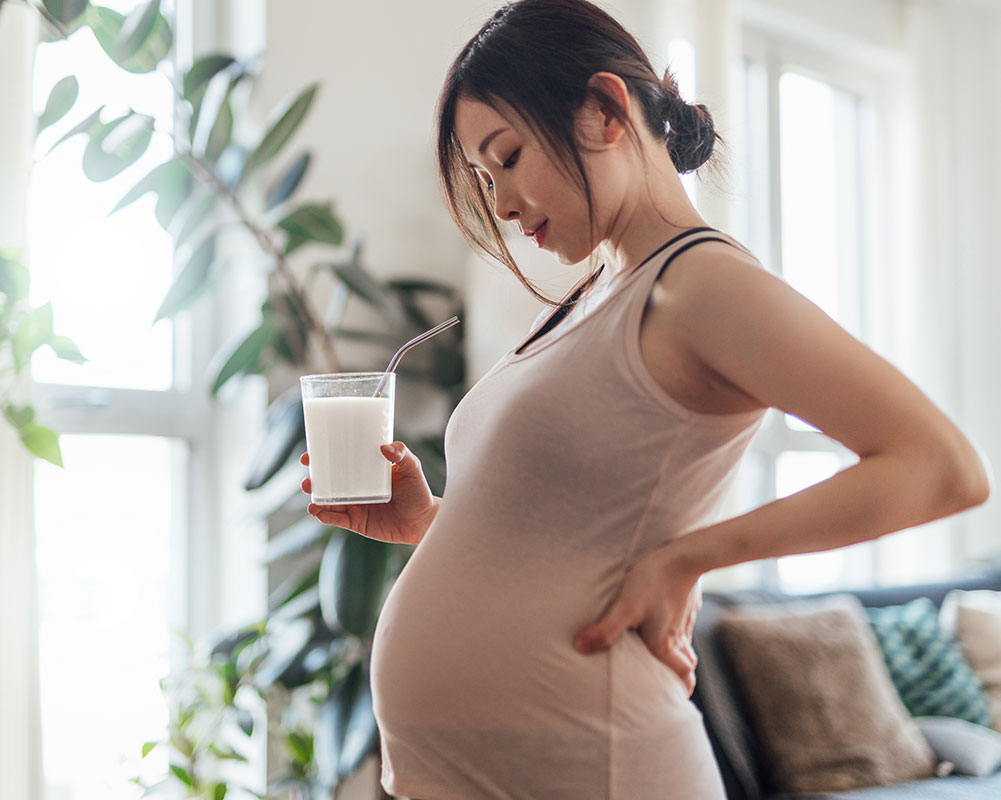 pregnant woman holding a glass of milk and looking at her stomach