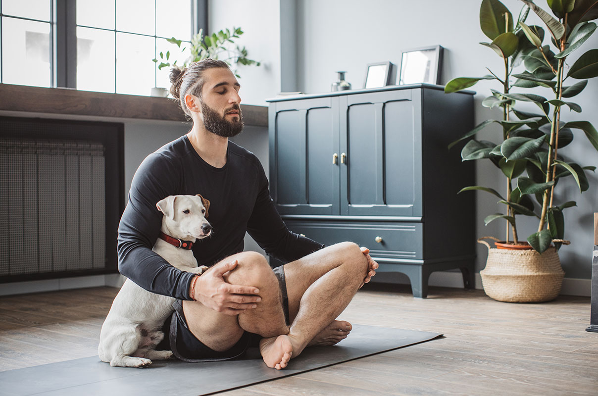 man practicing yoga at home with his dog