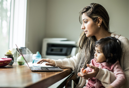 mother looking at laptop while young daughter sits on her lap