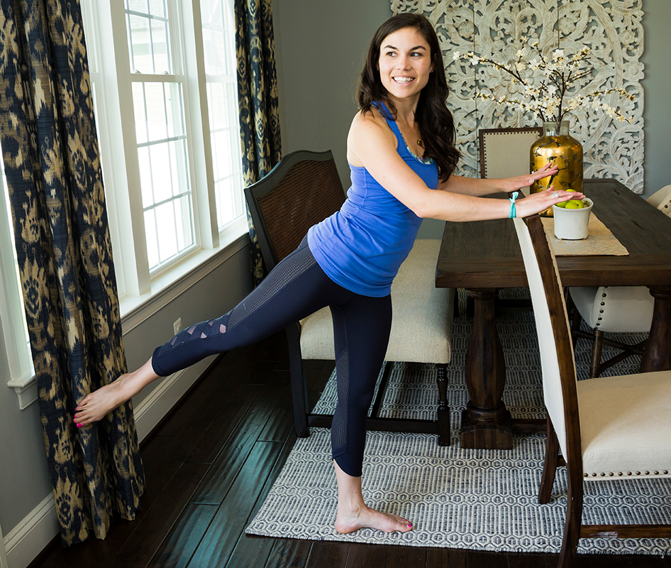 Woman holding on to her dining chair to perform Barre exercises at home.