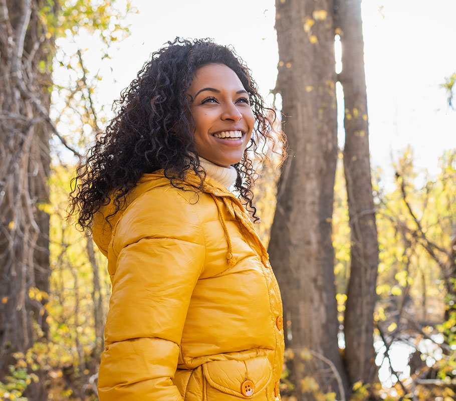 Woman in a yellow coat on a walk outside smiling into the distance towards the right