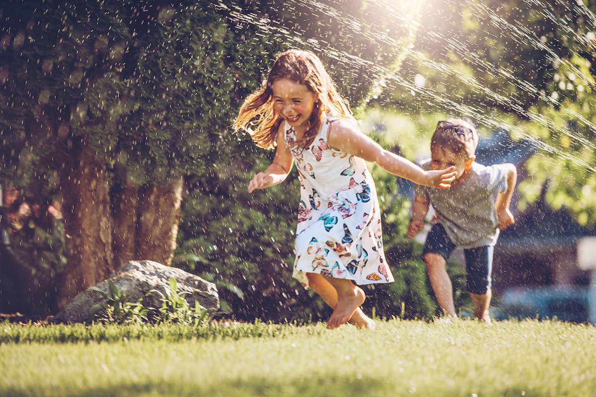 children playing running through a sprinkler outside
