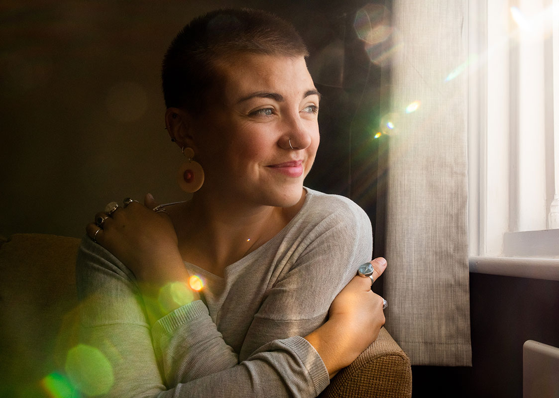 Woman embracing herself and smiling while looking out the window on the right