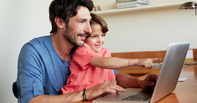 Dad on computer with child, using our member portal. 